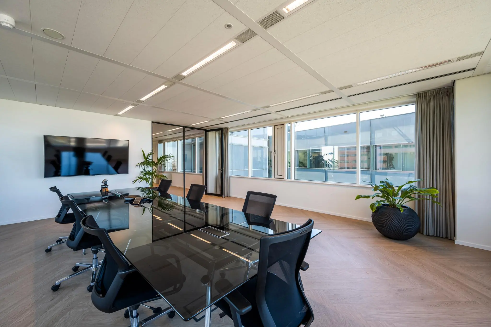 Moderne vergaderruimte aan de Thomas R. Malthusstraat met glazen tafel, bureaustoelen, grote tv en veel natuurlijk licht.